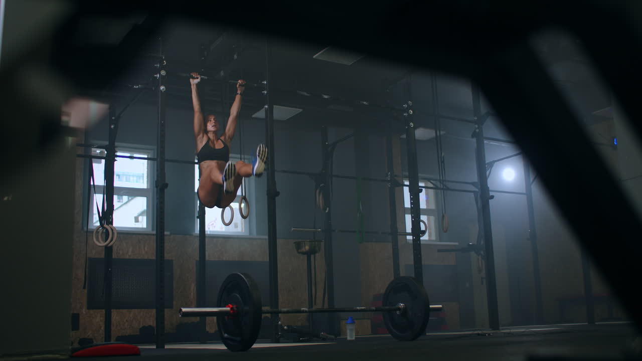 Slow motion: Raising feet up to bar on gym bar attractive muscle woman exercise and train in gym. Female athlete standing on a horizontal bar lifts her legs to train the muscles of the abs