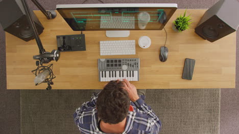 overhead view of male musician at workstation with keyboard and microphone in studio