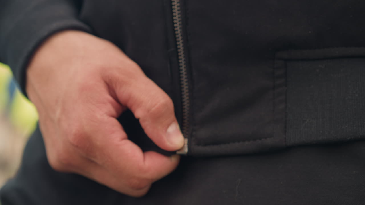 Primer plano de un hombre subiéndose la cremallera de la sudadera antes de correr, varón caucásico ajustándose la cremallera de la sudadera para hacer jogging matutino al aire libre, toma detallada de las manos subiendo la cremallera de una sudadera informal antes de correr al aire libre por la mañana