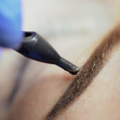master's hand is appling tattooing on the eyebrows of a woman with using a professional machine in a beauty salon. permanent makeup. close-up