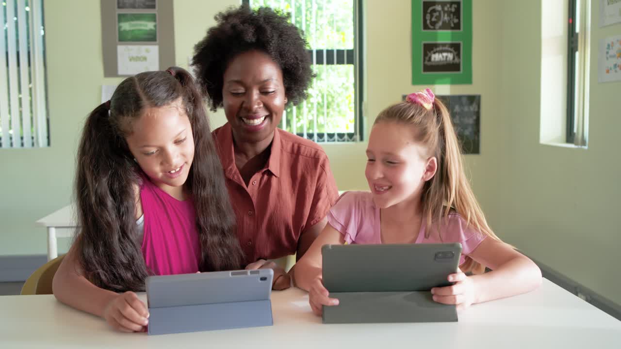 African-American teacher in rust top leaning in guiding two kids tapping blue gray tablets in class