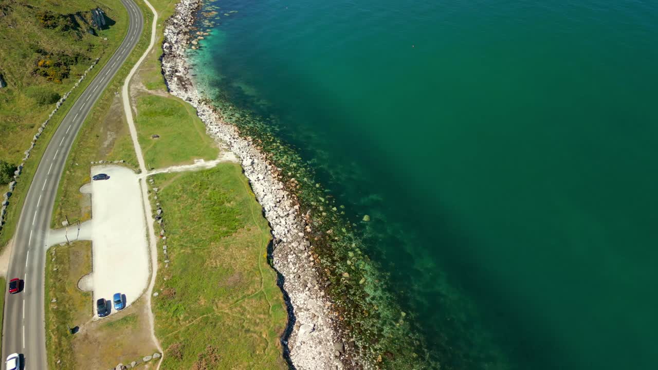 Overhead reversing aerial video of the Causeway Coastal Route in County Antrim, Northern Ireland, UK, on a bright and sunny day. Cars pass below. Filmed in 4K, 60FPS and with Rec709 color.