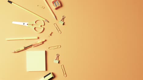 Overhead-view-of-school-stationery-with-copy-space-on-orange-background,-in-slow-motion