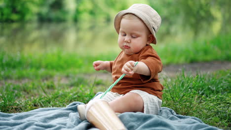 adorable cute toddler boy sits on the plaid. kid in a cap plays with a cup with a straw. blurred backdrop.