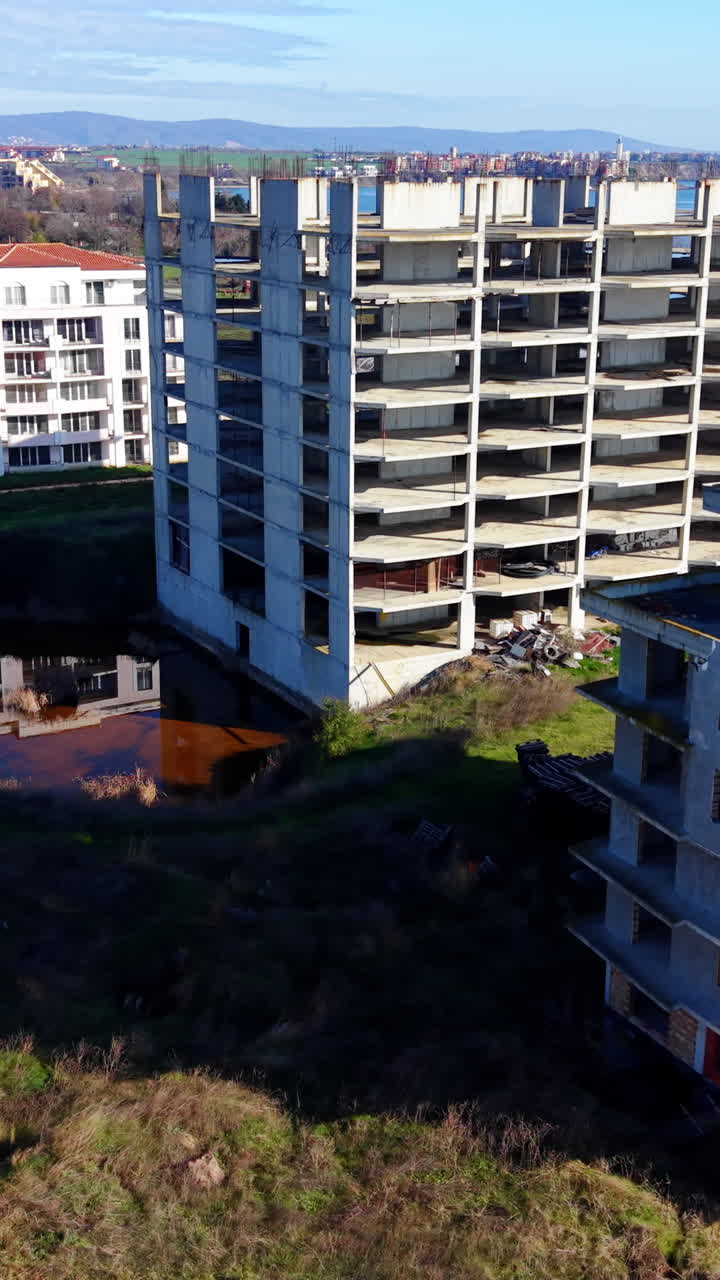 Veduta aerea dall'alto di grandi scheletri in cemento di edifici in un campo vicino al mare. Complesso edilizio multipiano abbandonato. Video verticale.