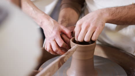 close up of male teacher helping man sitting at wheel in pottery class