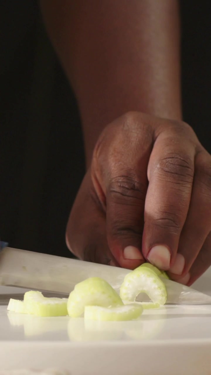 Vertical video: Slicing hand steadying pale green veg on board, cutting uniform slices with knife