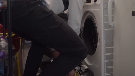 Young-Caucasian-man-puts-laundry-into-white-front-load-washing-machine