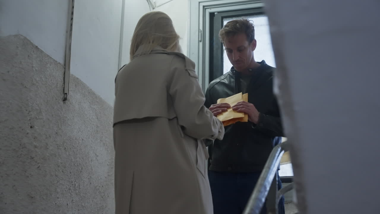 Woman and man meet in staircase of building to exchange envelope with cash or payment for service. Dark dirty deal or business. Fraud and collusion. Insider information and bribery. Spy network