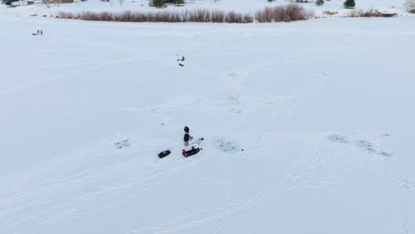 boseman montana ice fishermen on snowy frozen suburban pond, tracking right with 4k drone during golden hour