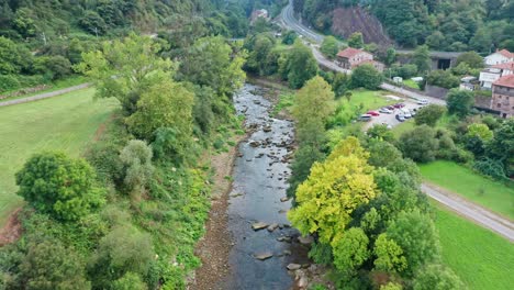 volando sobre un pequeño río en una aldea rural rodeada de árboles en españa