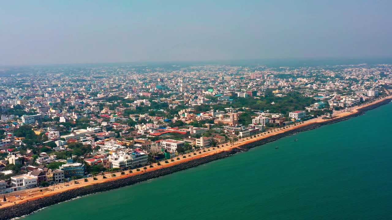 Goubert Beach Road Puducherry si estende lungo la costa del Golfo del Bengala con un denso sviluppo urbano nell'entroterra. Una ripresa aerea fluida rivela la passeggiata costiera e le case del quartiere residenziale