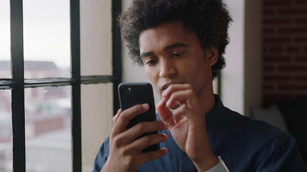 portrait attractive mixed race man using smartphone at home enjoying relaxed morning browsing messages texting social media looking out window planning ahead