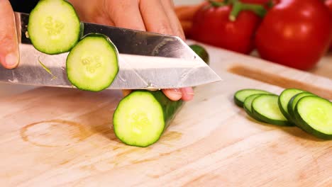 manos cortando pepino con tomates en el fondo