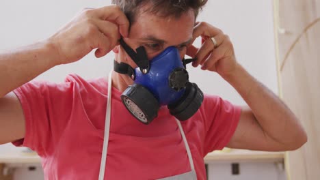 Caucasian-male-surfboard-maker-wearing-a-protective-apron-and-putting-on-a-face-mask