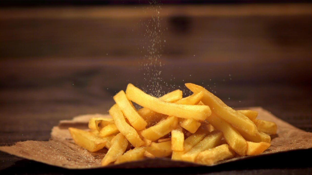 Salt Being Sprinkled on a Pile of Golden French Fries