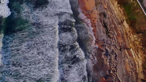 drone shot tilting up and filming the waves rolling in to a rocky beach in portugal