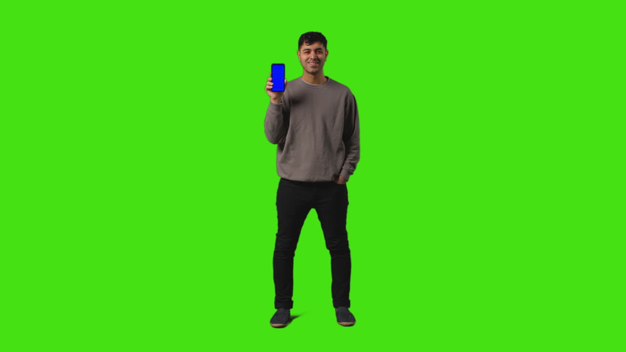 fotografía completa de un hombre sosteniendo un teléfono móvil de pantalla azul frente a la cámara contra un fondo de pantalla verde 1