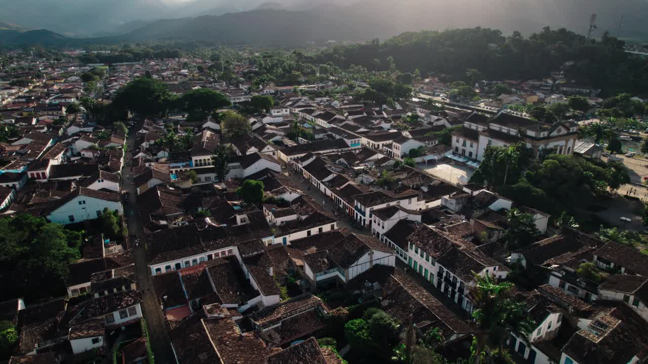 Paraty's UNESCO World Heritage Center. Features the distinct white-and-tile colonial architecture, cobblestone streets, and the lush Atlantic Forest mountains framing the town and its river channel