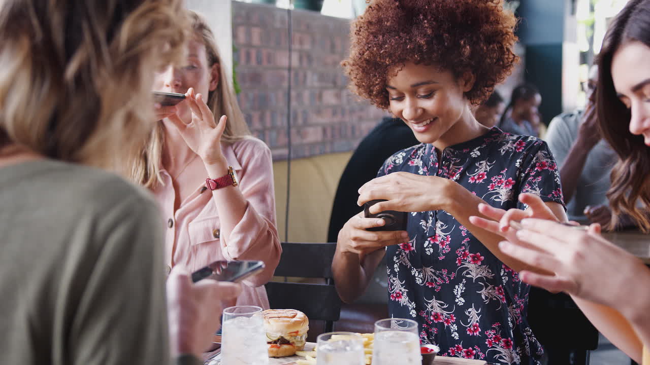 Quattro amiche che scattano foto al cibo in un ristorante da pubblicare sui social media.