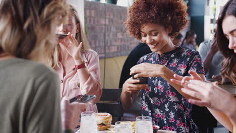 four female friends taking photos of food in restaurant to post on social media