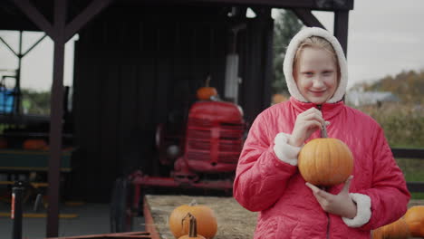 El-Niño-Sostiene-Una-Calabaza,-Se-Encuentra-En-Una-Granja-Cerca-De-Un-Tractor.-Vacaciones-De-Otoño-Y-Halloween