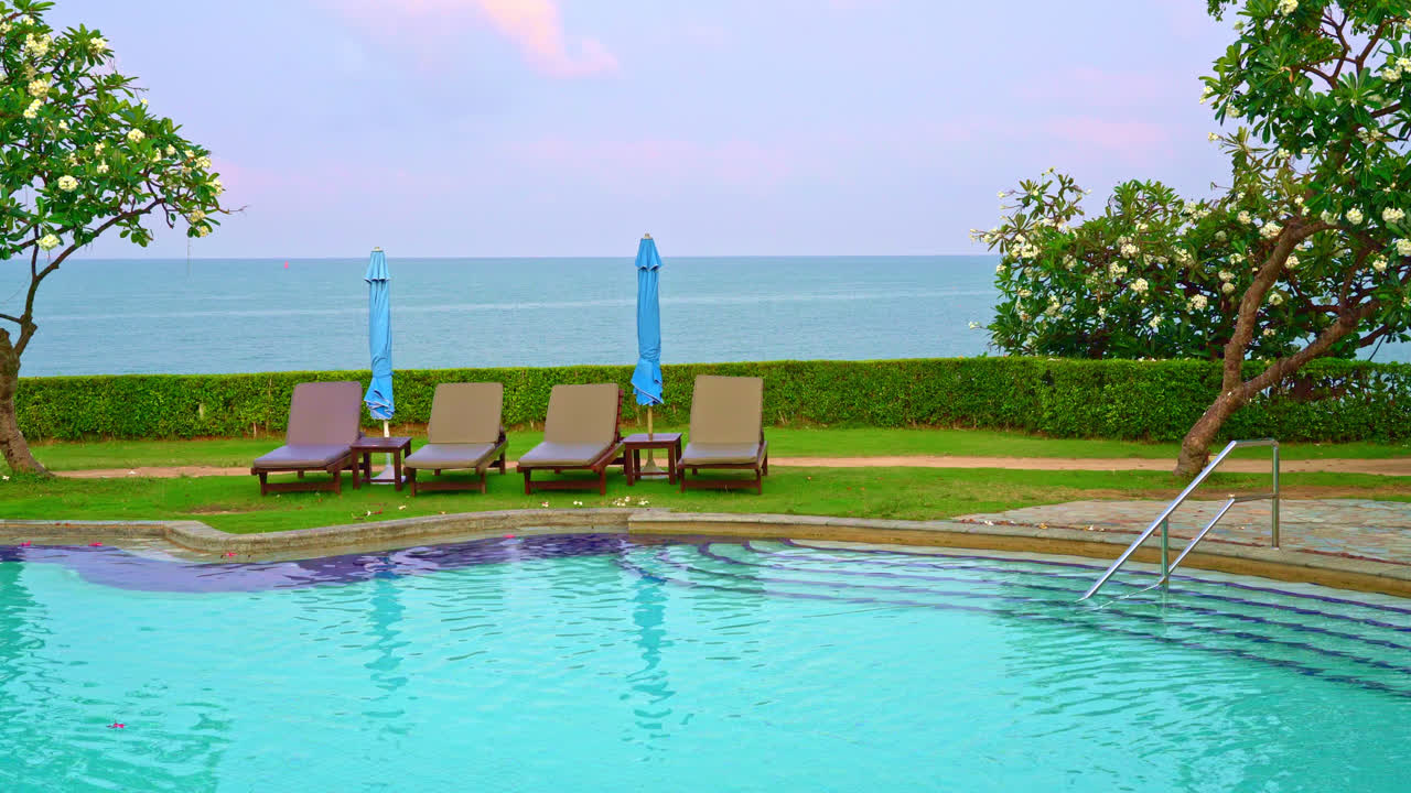 바다를 배경으로 한 수영장 주변의 의자 수영장 또는 침대 수영장과 우산 - 휴일 및 휴가 개념