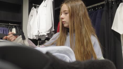 chica de pelo largo en la tienda de ropa navegando por los rieles de la ropa