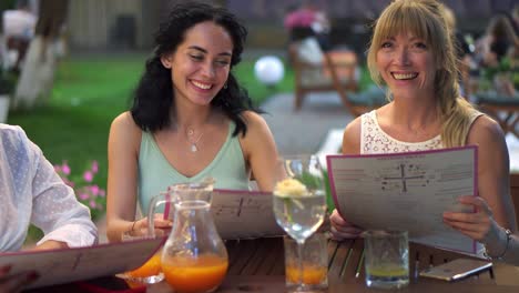 retrato de tres bonitas amigas leyendo el menú y divirtiéndose juntas en el café al aire libre en el parque público
