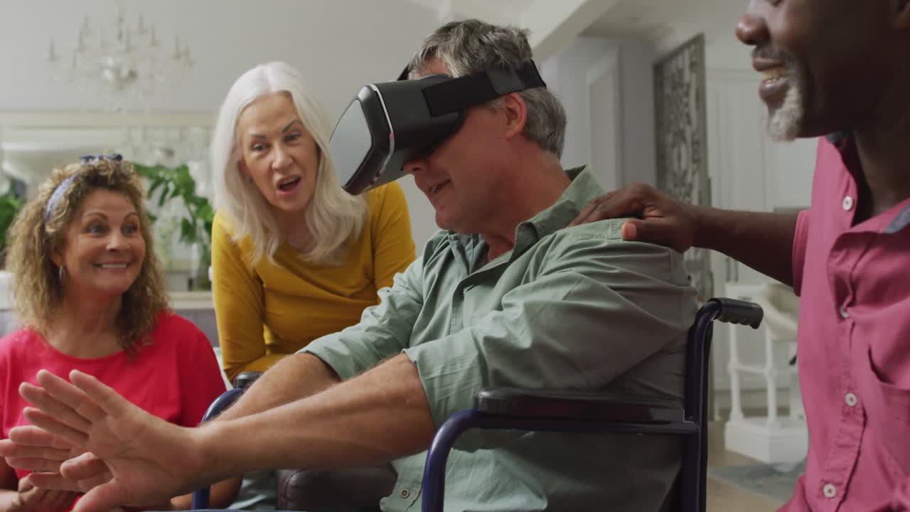Video di un uomo anziano felice in sedia a rotelle che usa un visore VR e si diverte con amici di diverse etnie.
