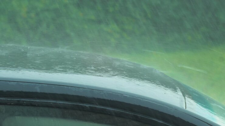 View of heavy storm hail and rain falling on a black car, nature disaster, climate changes, global warming, hot summer day, medium closeup shot