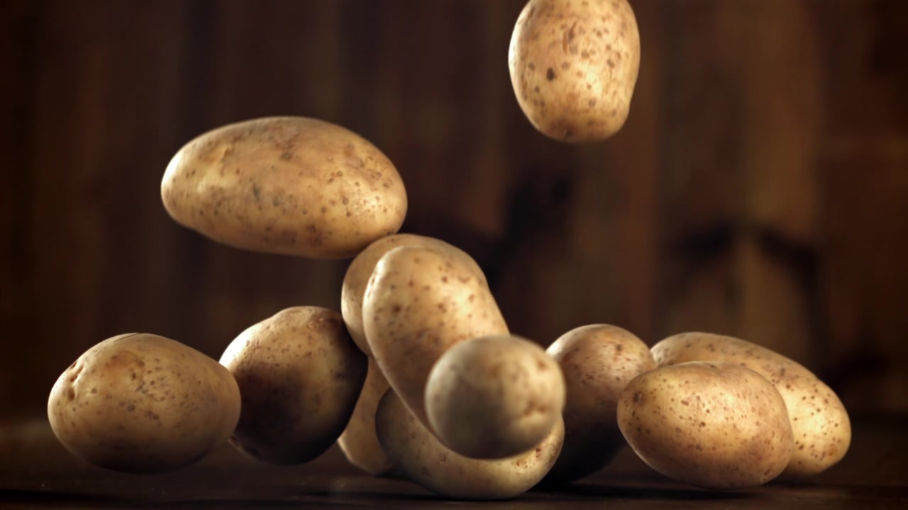 Patate crude che cadono e si depositano su una superficie di legno al rallentatore