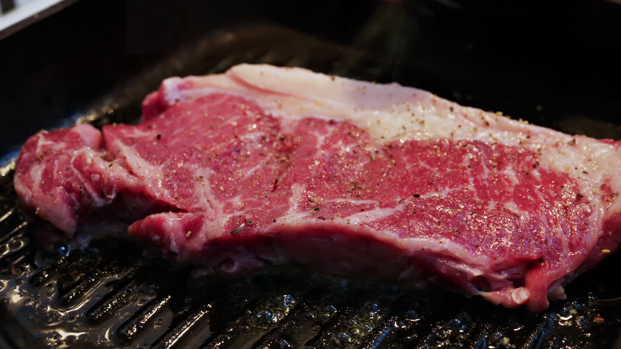 Fresh raw steak sizzling on a hot grill pan with visible seasoning and cooking oil