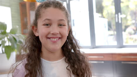 feliz chica biracial con el cabello largo y rizado de pie y sonriendo en la cocina soleada