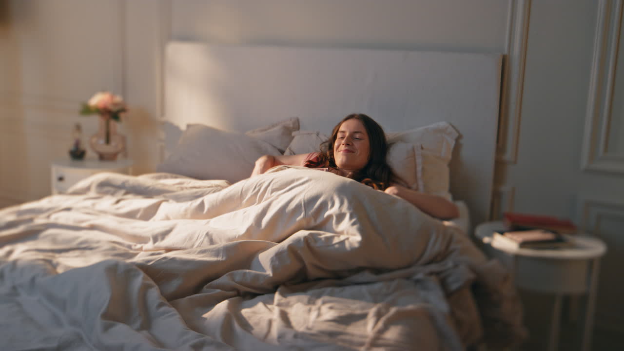 아침 소녀는 빛에 침대를 펴고 평화로운 긍정적 인 모델이 일찍 깨어납니다.