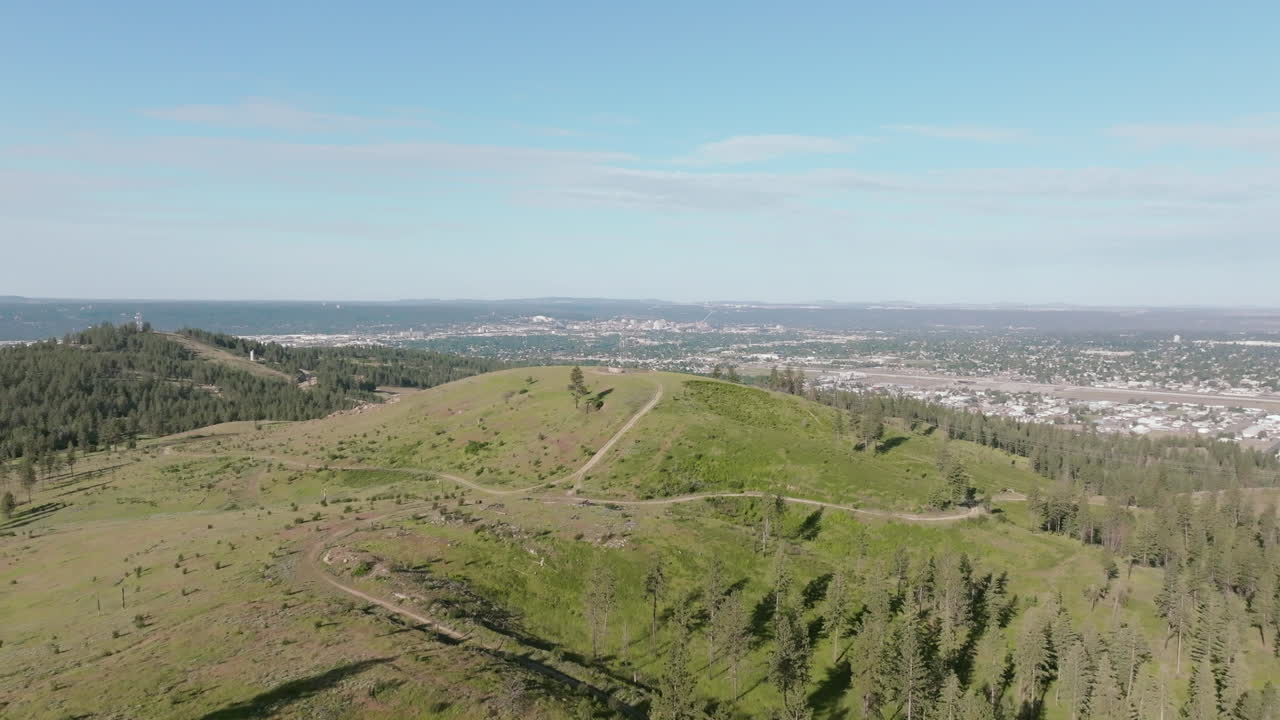 Aerial view of grassy rolling hills near Spokane with distant views of the city skyline under blue skies