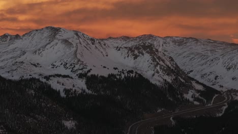 rocky mountains winter solstice colorado vibrant orange cloudy skies setting sunset aerial drone i70 highway cars trucks traffic coon hill parshall eisenhower tunnel continental divide forward pan up