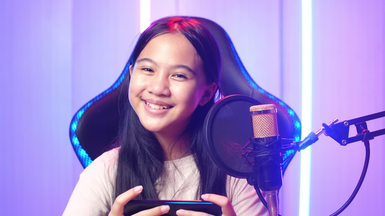Excited Asian Kid Girl Playing Video Game With Mobile Phone Then Smiles To Camera While Live Stream