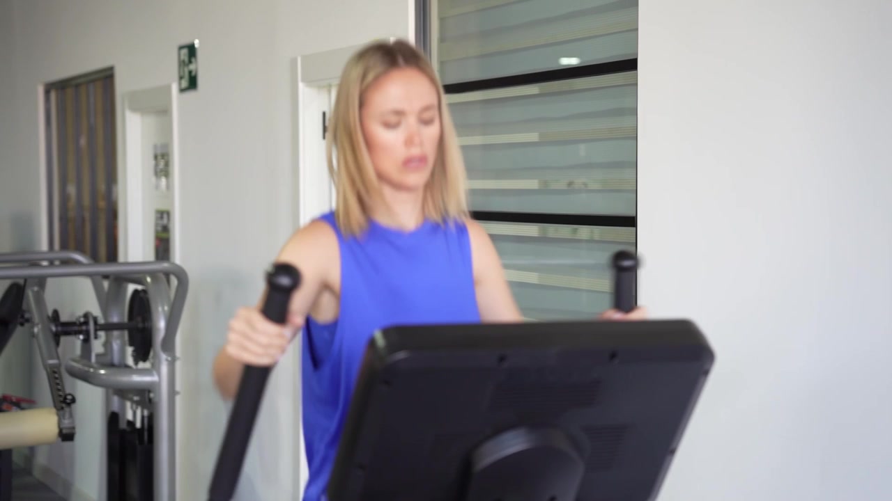 Una donna che si allena su una macchina ellittica in palestra mostrando impegno per la salute e il fitness.