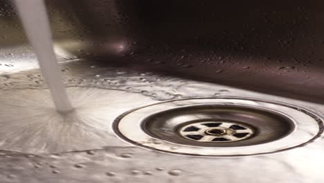 close-up of water flowing into a stainless steel sink