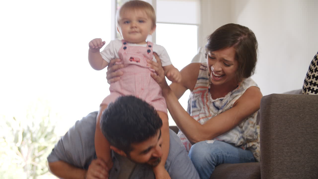 Parents Playing With Baby Son On Sofa At Home