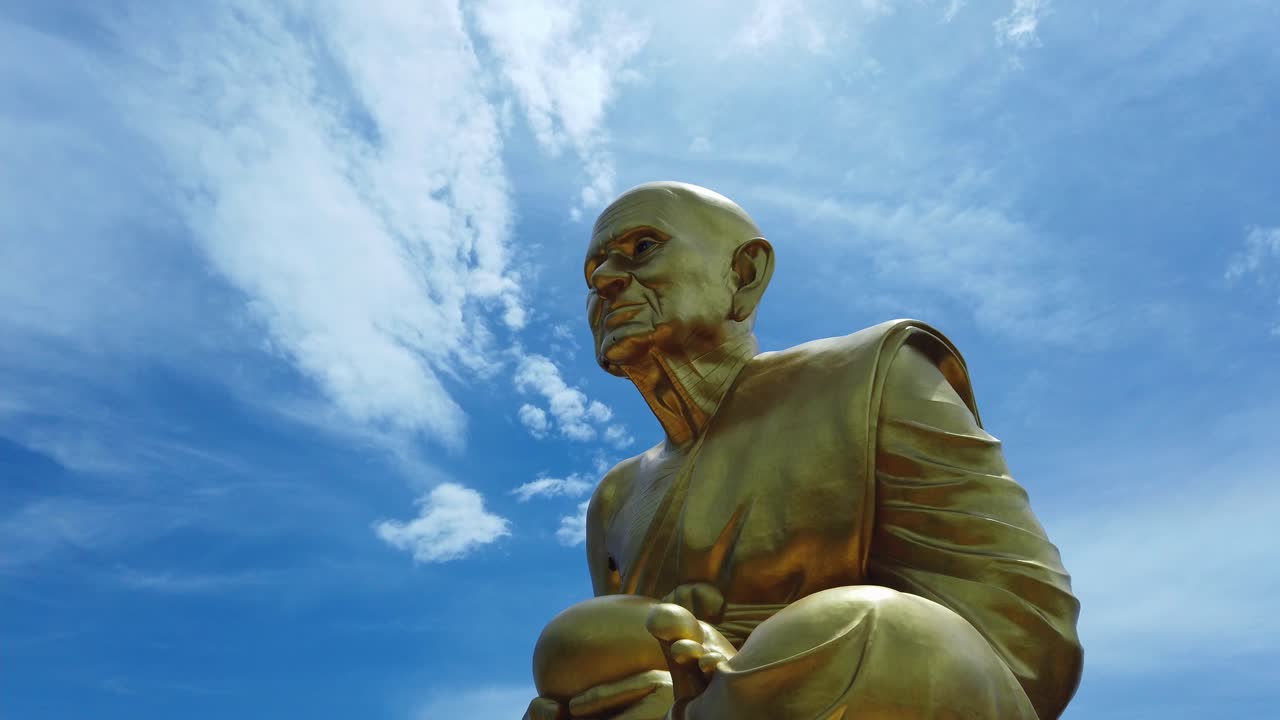 enorme estatua dorada del monje luang pu thuat, el discípulo del señor buddha en su posición de meditación contra el cielo azul y el fondo de las nubes cirrocúmulos en phuttha utthayan maharat ayutthaya tailandia
