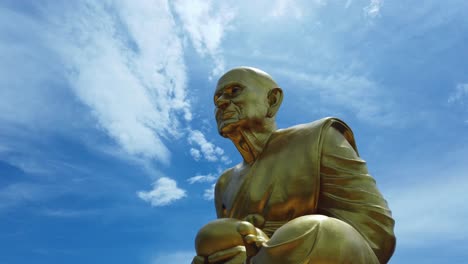 huge golden statue of monk luang pu thuat, the disciple of lord buddha in his meditation position against blue sky and cirrocumulus clouds background in phuttha utthayan maharat ayutthaya thailand