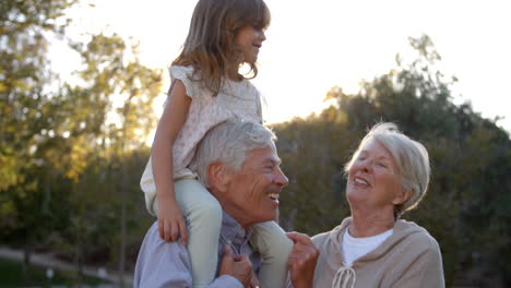 grandparents giving granddaughter a shoulder ride in park