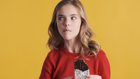 teenage caucasian girl eating chocolate bar and nodding.