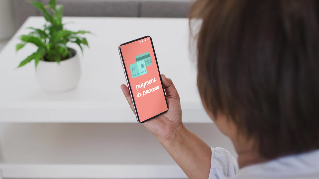 mujer biracial usando teléfono inteligente en casa compras en línea con pago en proceso, cámara lenta