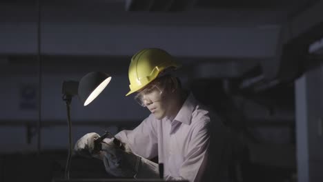 joven ingeniero asiático que trabaja y utiliza herramientas de medición de la calidad de las piezas metálicas. hombre que usa casco de seguridad con taller de trabajo. concepto de ingeniería, carrera, industria, fabricación, seguridad