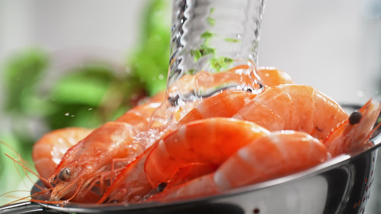 lavando camarones blanqueados rojos en un colander bajo una corriente de agua salpicando en cámara lenta