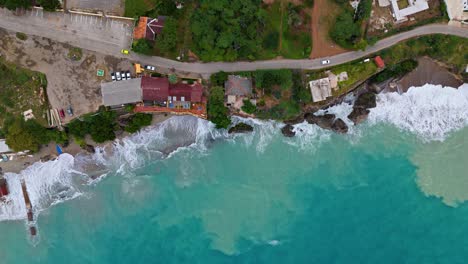 Drone-De-Arriba-Hacia-Abajo-A-Lo-Largo-De-Una-Carretera-Costera-Con-Casas-Mientras-La-Arena-Se-Agita-Debido-A-Fuertes-Olas-En-El-Caribe