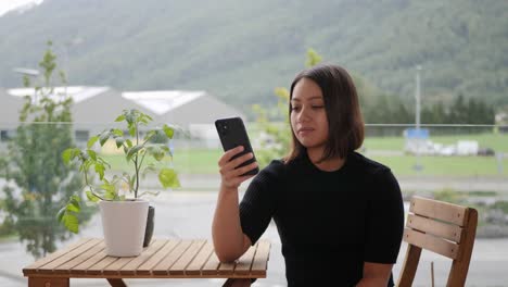 Lonely-Thai-woman-looking-at-her-phone-in-her-urban-garden-in-loud-city-traffic